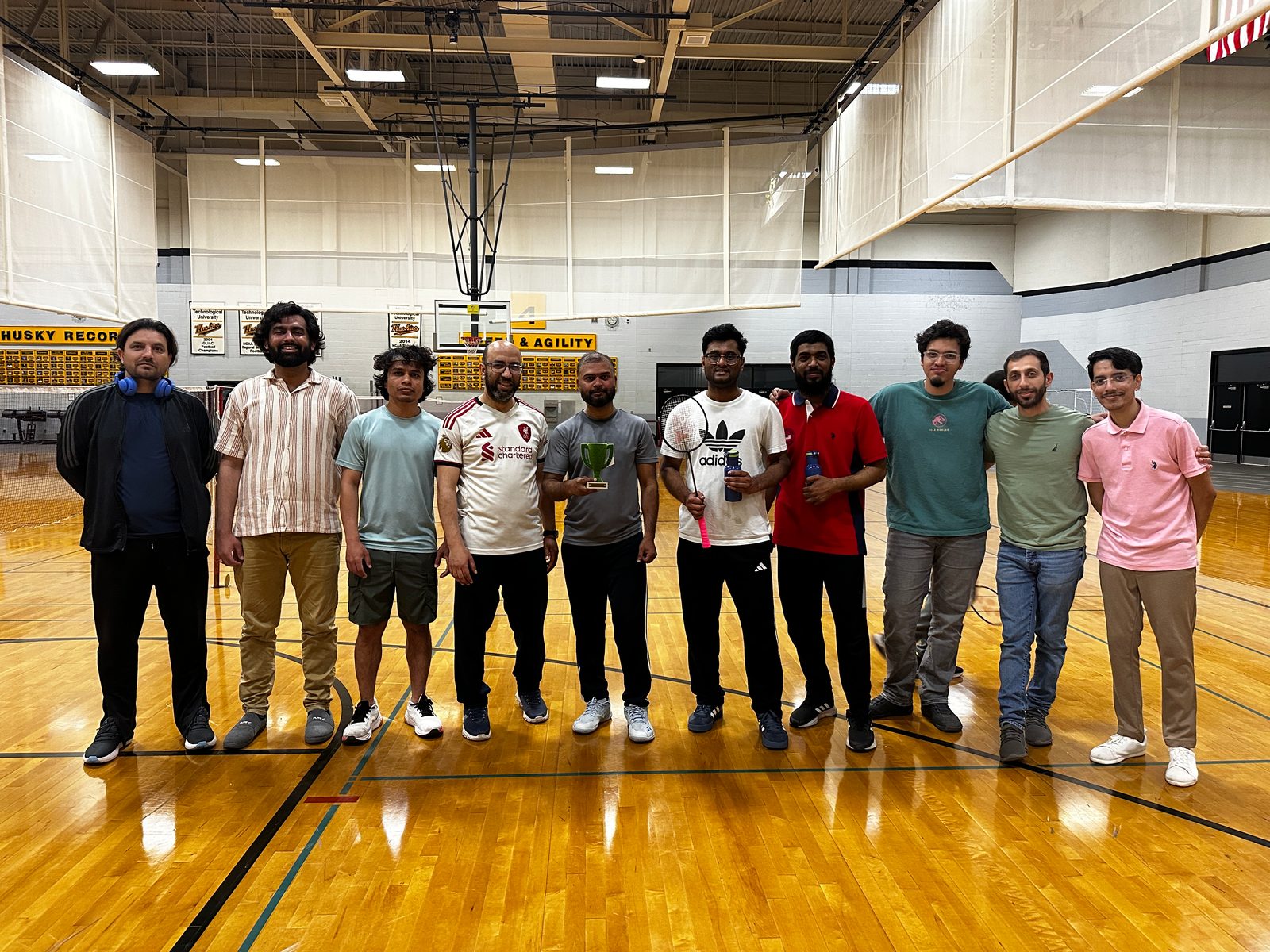 Players line up for a group photo on the gym floor, one holding the trophy.