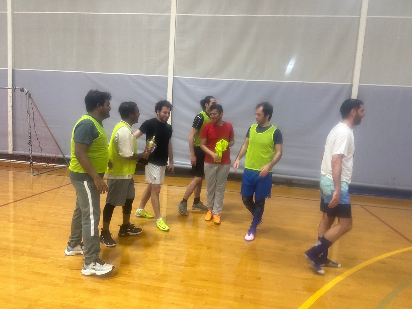 Players, most in yellow bibs, stand together on the gym floor as one holds a gold trophy.