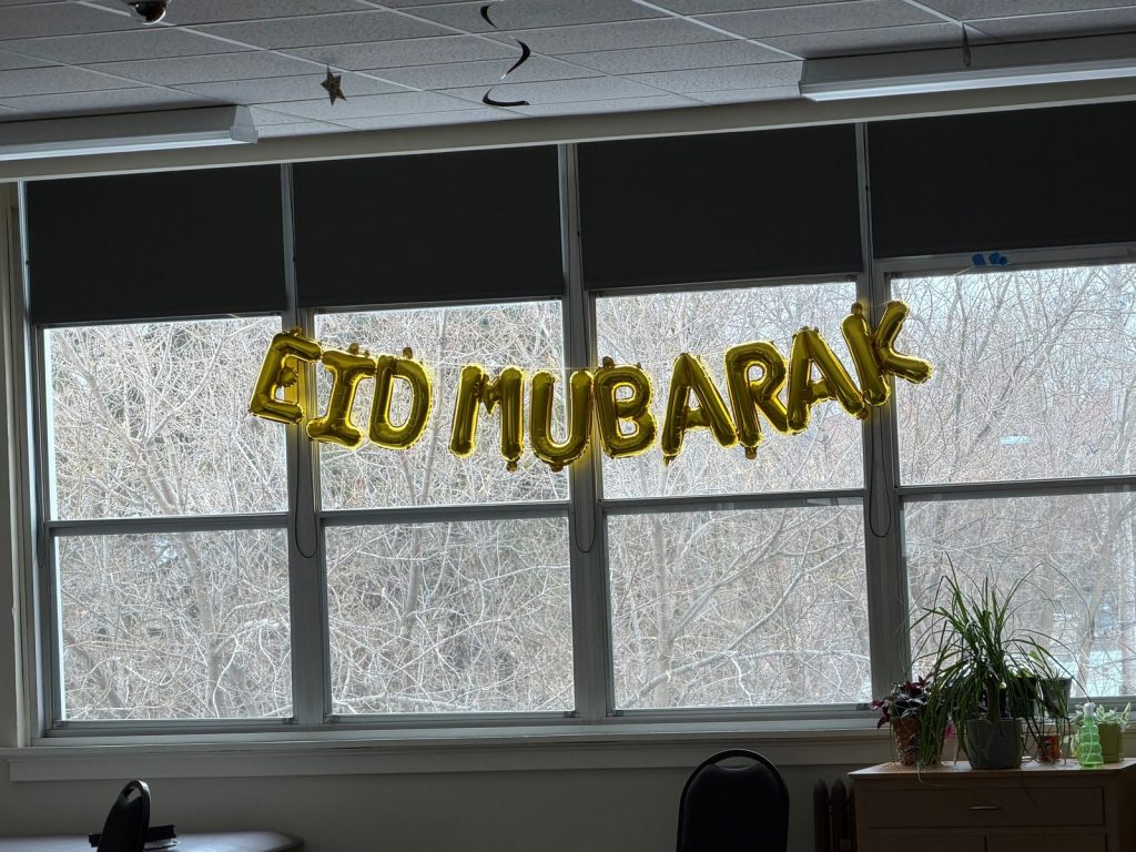 Gold balloon letters spelling Eid Mubarak hang across a window in the meal hall.