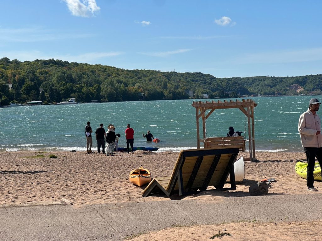 People gather at the shoreline of a wind-whipped lake as one person wades beside a kayak in the water.