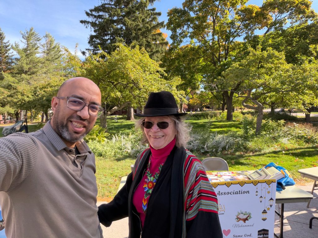 A man from the MSA table takes a smiling selfie with a visitor in a black hat and sunglasses.
