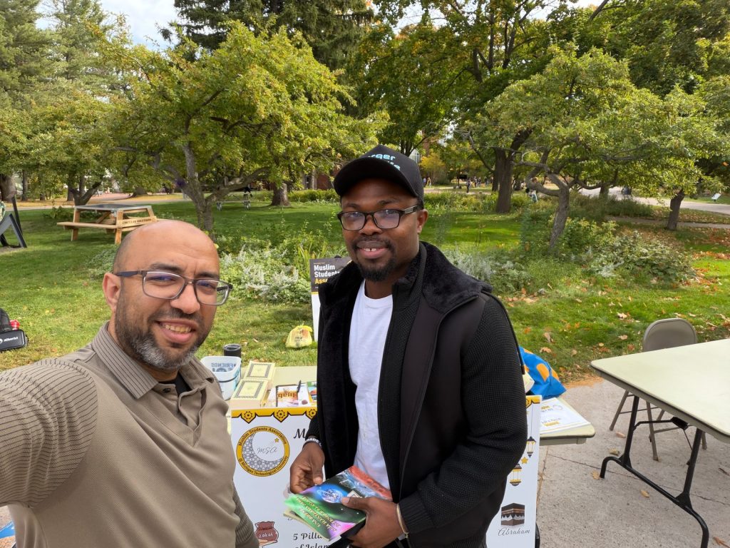 A man from the MSA table and a visitor holding booklets smile for a selfie in front of the table.