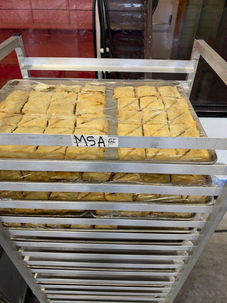 Plastic-wrapped trays of baklava on a metal rack labeled MSA.